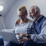 Elderly couple looking at a laptop screen and smiling.