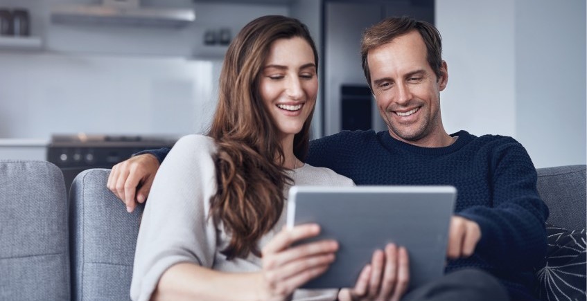 Man and woman hugging and smiling while looking at a tablet