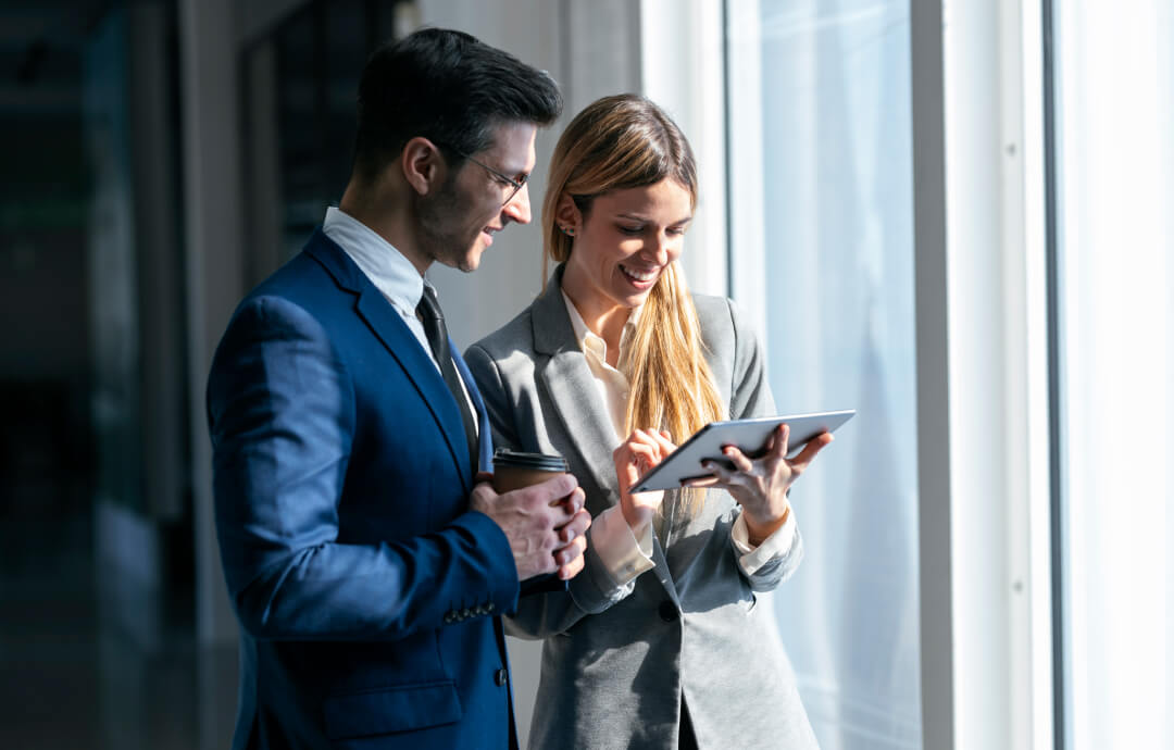 Businessman and businesswoman smiling while looking at a tablet.