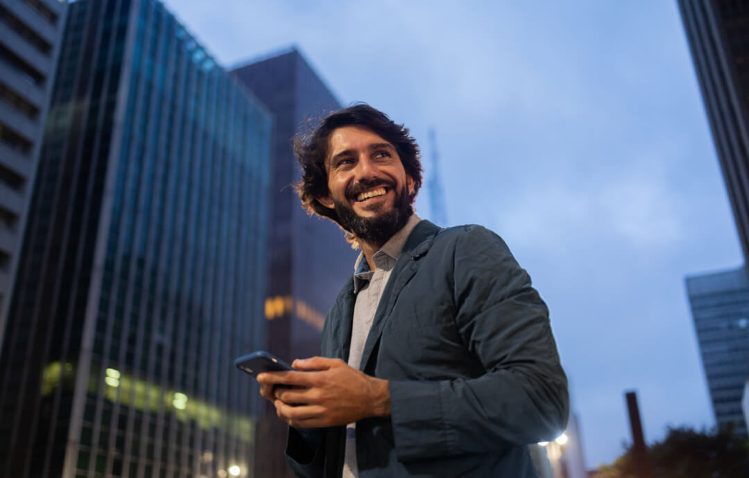 Smiling man holding phone in urban area at dusk.