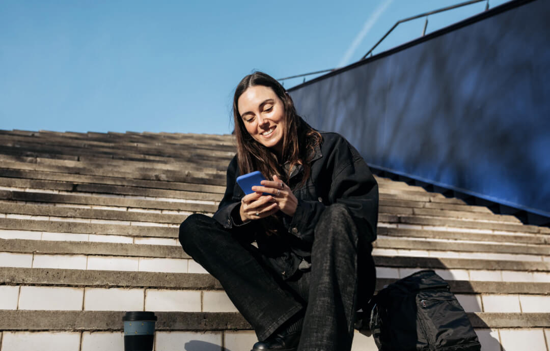 Young woman sitting on stairs, smiling while using her phone.