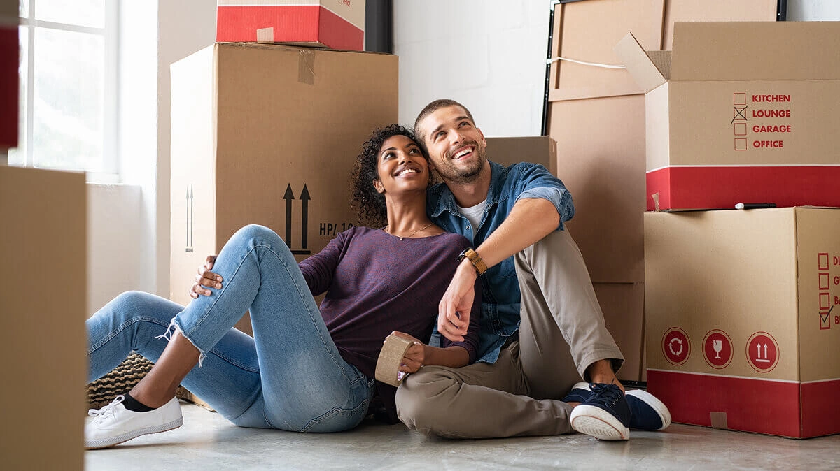 Man and woman smiling while leaning on cardboard boxes.