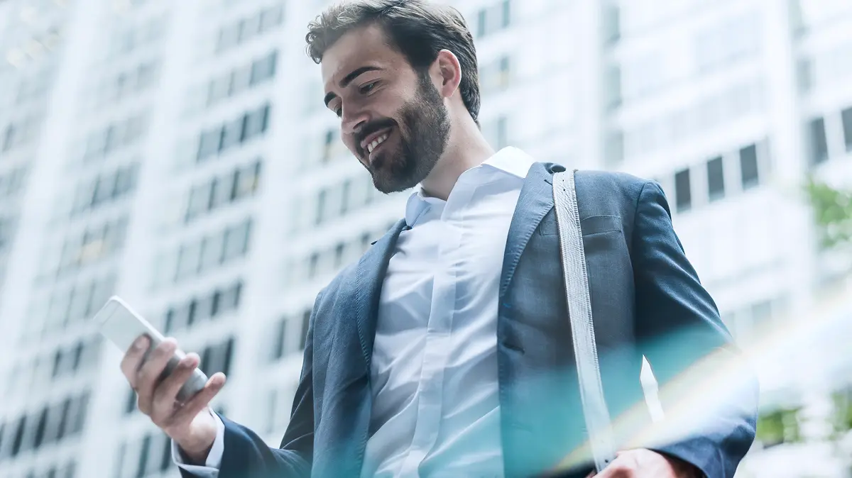 Man in a suit smiling while looking at his cell phone screen.